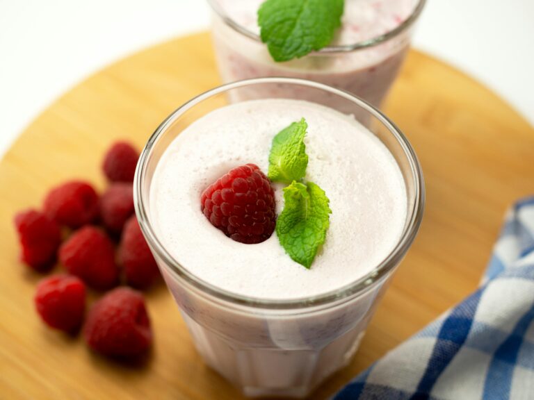 Een romige smoothies maken met yoghurt, versierd met stukjes banaan en rood diepvriesfruit, geserveerd in een glazen pot met een rietje.